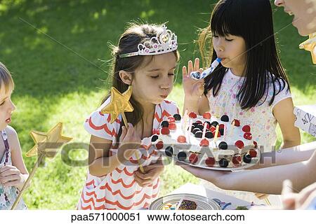 Girl blowing out candles on birthday cake at outdoor birthday party View Large Photo Image Stock Image - Girl blowing out candles on birthday cake at outdoor birthday party. Fotosearch