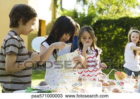 Stock Image - Girl opening gift at birthday party as friends watch. Fotosearch