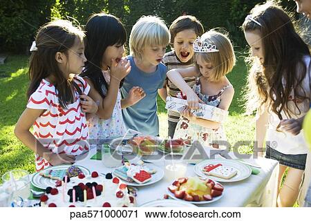 Stock Image - Girl opening gift at birthday party as friends watch. Fotosearch