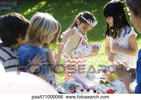 Girl opening gift at birthday party as friends watch View Large Photo Image Stock Photograph - Girl opening gift at birthday party as friends watch. Fotosearch