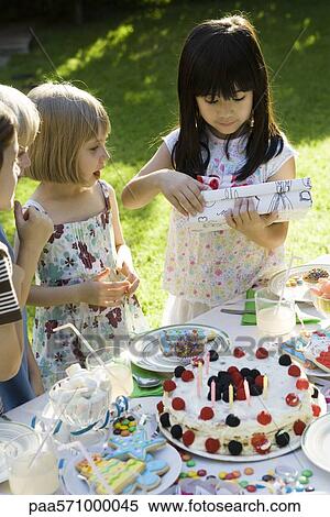 Stock Photography - Girl opening gift at birthday party as friends watch. Fotosearch