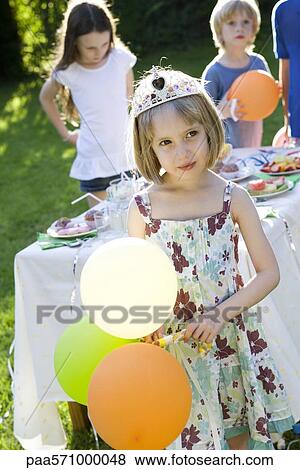 Stock Photo - Girl wearing tiara and holding balloons at outdoor party. Fotosearch