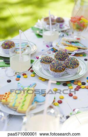 Stock Image - Iced cookies and cupcakes on table decorated with streamers and candy. Fotosearch