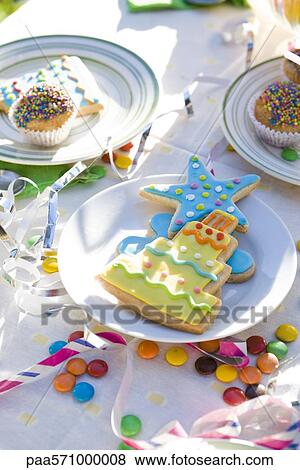 Stock Photo - Iced cookies, cupcakes on table decorated with streamers and candy. Fotosearch