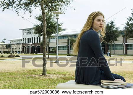 Female student sitting on bench on school campus View Large Photo Image Stock Photograph - Female student sitting on bench on school campus. Fotosearch