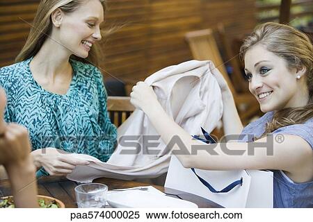 Friends together in outdoor cafe, one woman showing new clothing in shopping bag View Large Photo Image Stock Photography - Friends together in outdoor cafe, one woman showing new clothing in shopping bag. Fotosearch