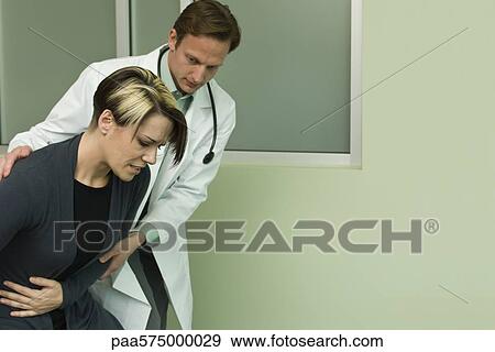 Doctor assisting patient experiencing severe abdominal pain View Large Photo Image Stock Photo - Doctor assisting patient experiencing severe abdominal pain. Fotosearch