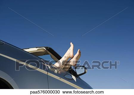 Stock Image - Relaxing in parked convertible, feet resting on door. Fotosearch