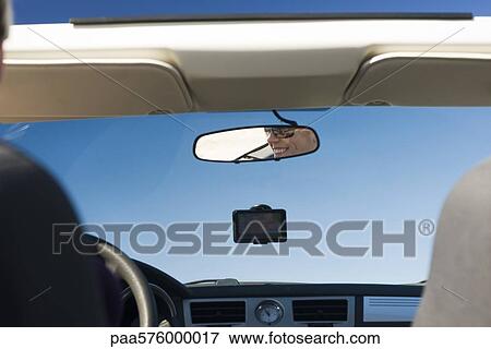 Stock Photo - Woman driving car, reflection in rearview mirror. Fotosearch