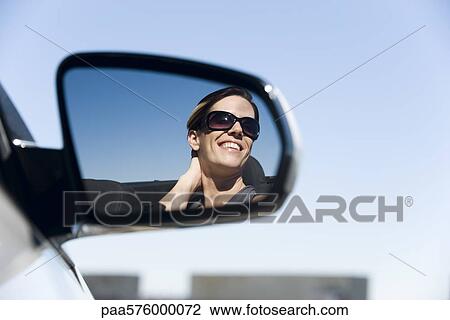 Stock Image - Woman passenger in car, reflection in side-view mirror. Fotosearch