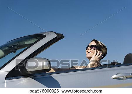 Woman talking on cell phone while driving convertible View Large Photo Image Stock Photograph - Woman talking on cell phone while driving convertible. Fotosearch