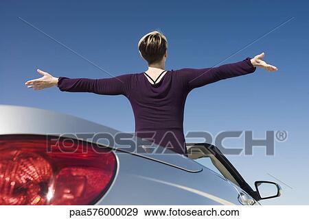 Woman with arms outstretched standing in parked convertible enjoying the outdoors View Large Photo Image Stock Photo - Woman with arms outstretched standing in parked convertible enjoying the outdoors. Fotosearch