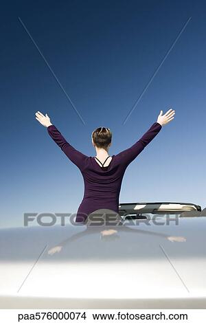 Woman with arms raised standing in parked convertible enjoying the outdoors View Large Photo Image Picture - Woman with arms raised standing in parked convertible enjoying the outdoors. Fotosearch