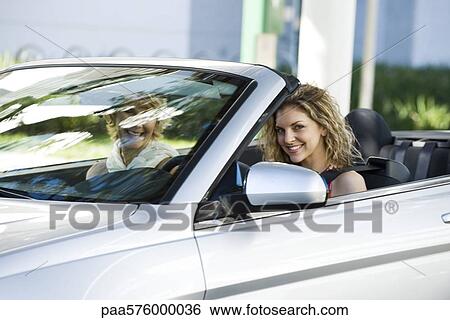 Stock Photograph - Young woman driving convertible with friend. Fotosearch