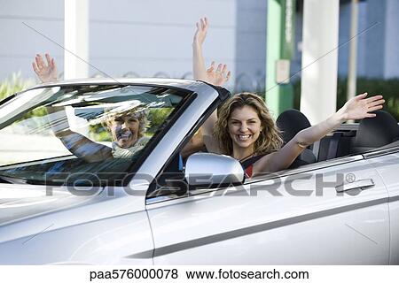 Young woman with friend in convertible with look of excitement and arms raised View Large Photo Image Stock Photo - Young woman with friend in convertible with look of excitement and arms raised. Fotosearch