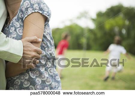 Close-up of couple embracing, children playing in background View Large Photo Image Stock Photo - Close-up of couple embracing, children playing in background. Fotosearch