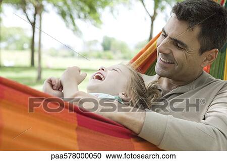 Stock Image - Father and daughter relaxing together in hammock, both laughing. Fotosearch
