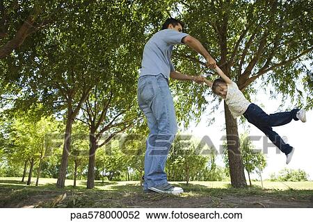 Stock Image - Father swinging his young daughter by her arms. Fotosearch