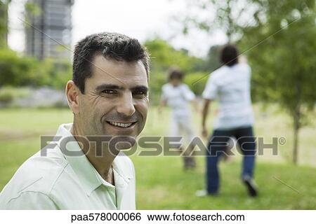 Man smiling at camera, sons playing in background View Large Photo Image Stock Photograph - Man smiling at camera, sons playing in background. Fotosearch