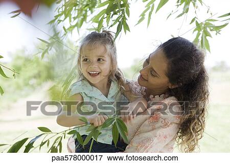 Mother holding young daughter outdoors, girl holding onto tree branch View Large Photo Image Stock Photo - Mother holding young daughter outdoors, girl holding onto tree branch. Fotosearch