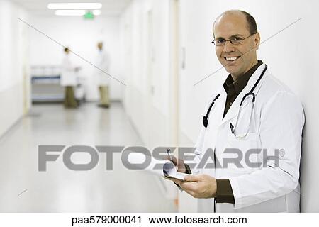 Stock Image - Doctor leaning against wall, portrait. Fotosearch