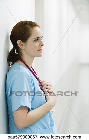 Stock Photo - Nurse leaning against wall, portrait. Fotosearch