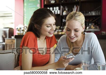 Female friends looking at cell phone together View Large Photo Image Stock Photo - Female friends looking at cell phone together. Fotosearch