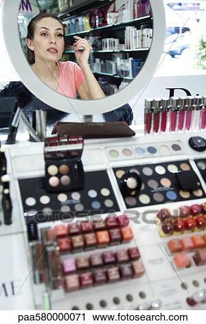 Stock Image - Young woman applying mascara in store. Fotosearch