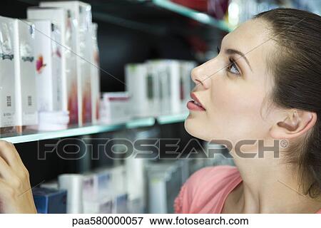 Young woman browsing shelf with cosmetics View Large Photo Image Stock Photo - Young woman browsing shelf with cosmetics. Fotosearch