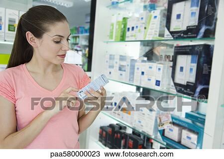 Stock Image - Young woman looking at cosmetics in store. Fotosearch