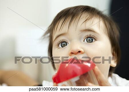 Stock Photo - Baby girl chewing on plastic cup. Fotosearch
