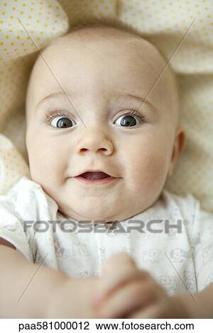 Stock Image - Infant looking at camera with wide eyes, portrait. Fotosearch