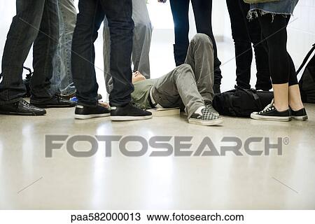 Stock Image - Bullies surrounding and threatening teenage boy lying on floor. Fotosearch