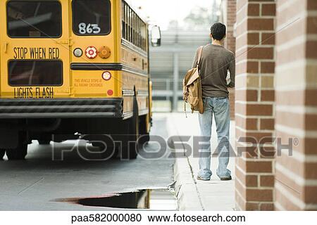 Stock Image - High school student waiting outside school for bus. Fotosearch