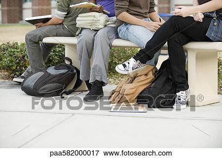 Stock Photo - Students hanging out together, sitting on park bench. Fotosearch