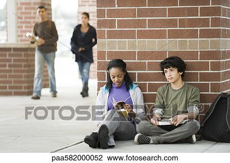 Stock Image - Students sitting together on sidewalk outside school. Fotosearch