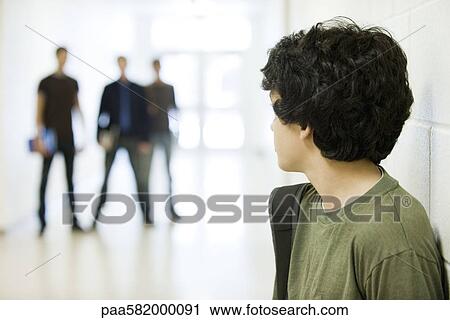 Teenage boy looking over shoulder at bullies in background View Large Photo Image Stock Image - Teenage boy looking over shoulder at bullies in background. Fotosearch