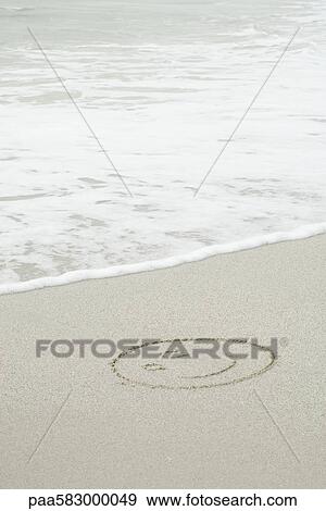 Stock Photo - Smiley face drawn in sand on beach. Fotosearch