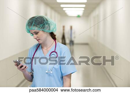 Nurse in hospital corridor using cell phone View Large Photo Image Picture - Nurse in hospital corridor using cell phone. Fotosearch