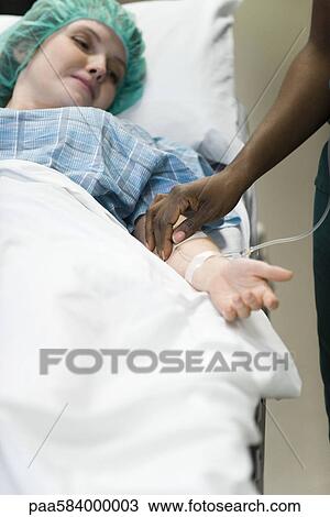 Stock Image - Patient watching as nurse checks IV needle placement in arm. Fotosearch