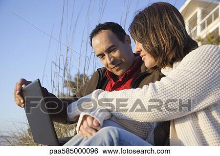 Stock Photograph - Couple using laptop computer at the beach. Fotosearch