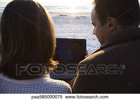 Couple using laptop computer together at the beach View Large Photo Image Stock Photography - Couple using laptop computer together at the beach. Fotosearch