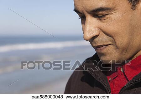 Stock Photo - Man at the beach looking down in thought, portrait. Fotosearch