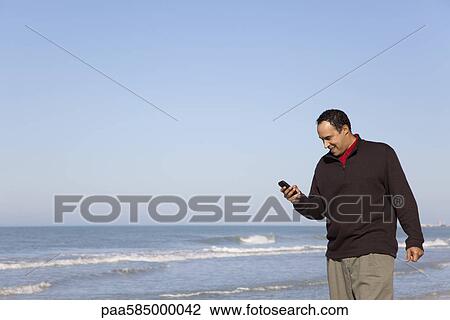Man looking text messaging on cell phone at the beach View Large Photo Image Stock Image - Man looking text messaging on cell phone at the beach. Fotosearch