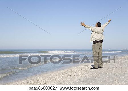 Man standing on beach looking at ocean with arms out View Large Photo Image Stock Photo - Man standing on beach looking at ocean with arms out. Fotosearch