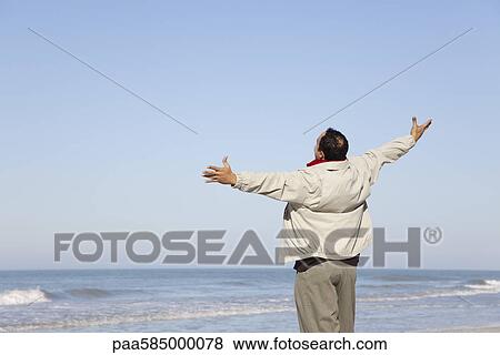 Man standing on beach looking at ocean with arms out View Large Photo Image Stock Photo - Man standing on beach looking at ocean with arms out. Fotosearch