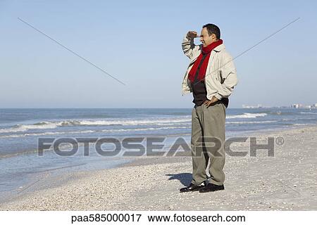 Stock Photo - Man standing on beach looking at view. Fotosearch