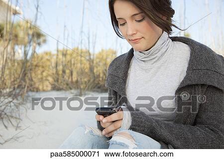 Stock Image - Teen girl text messaging at the beach. Fotosearch