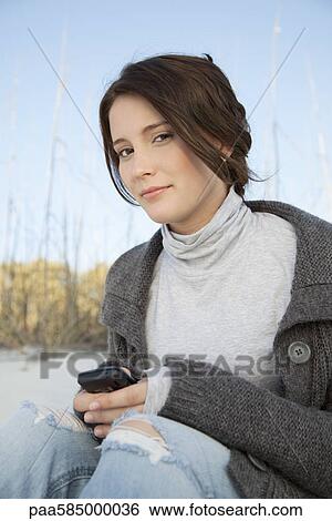 Stock Photograph - Teen girl text messaging at the beach, portrait. Fotosearch