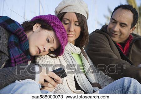 Teenage girl sitting outdoors with parents, text messaging with her cell phone View Large Photo Image Stock Image - Teenage girl sitting outdoors with parents, text messaging with her cell phone. Fotosearch